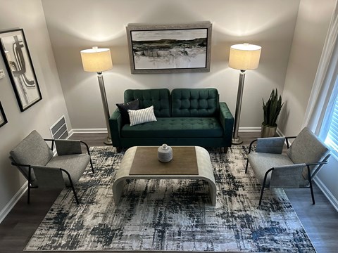 A living room with a green couch, two chairs, a coffee table, and a rug at Chelsea Place Apartments, Lithonia, GA, 30058