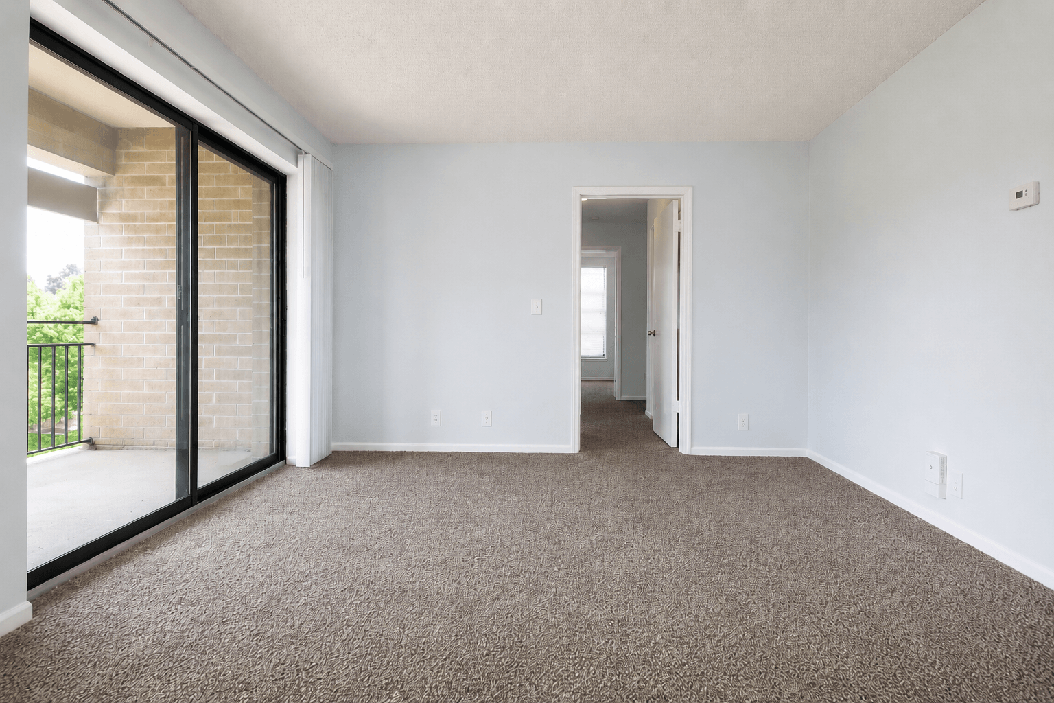 A large, empty room with a carpeted floor and a doorway leading to another room.