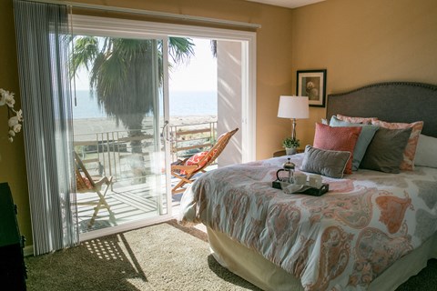 A bedroom with a large bed and a view of the beach through the sliding glass door.
