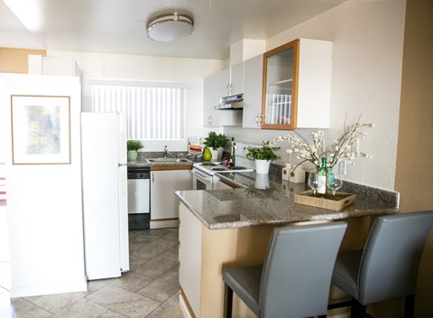 A kitchen with a white fridge, a sink, a counter and a dining table.