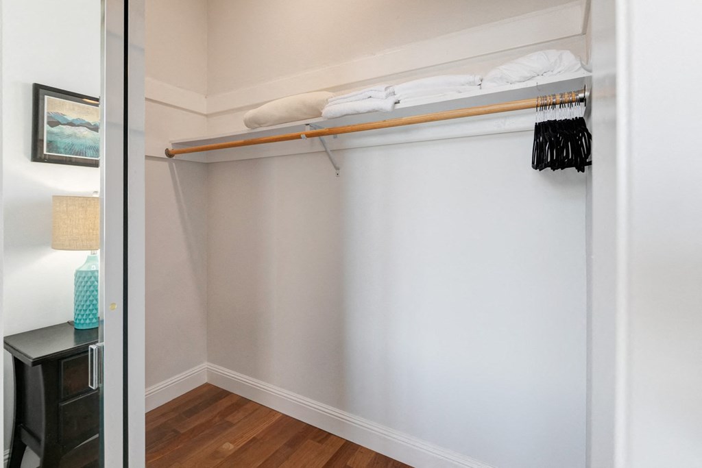 a closet with a white wall and a shelf with clothes on it and a mirror