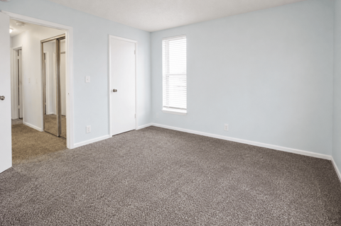 A room with a carpeted floor and a window with blinds.