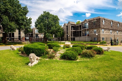 A stone lion statue sits in a green grassy area in front of a building.