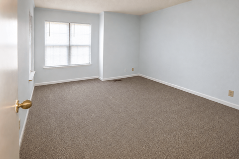 A room with a carpeted floor and a window with blinds.