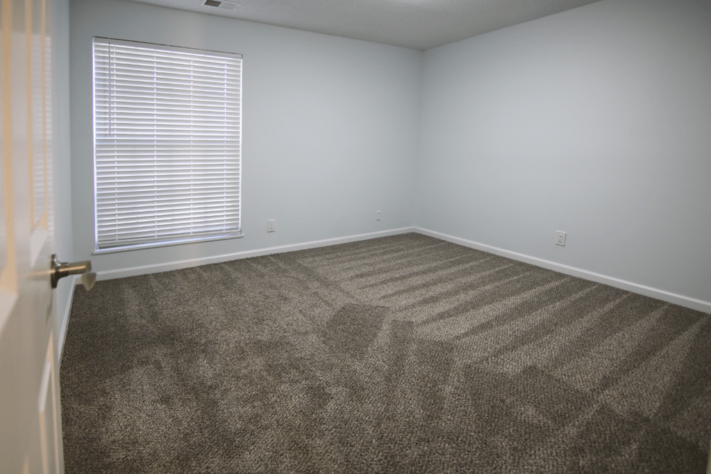 A room with a carpeted floor and a window with blinds.