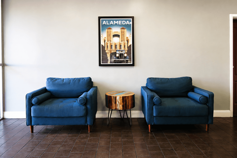 Two blue chairs and a small table are in a room with a poster on the wall.