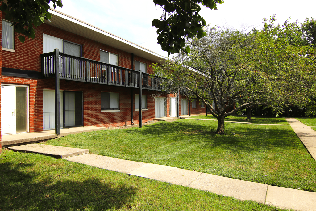 A red brick building with a balcony and a tree in front.