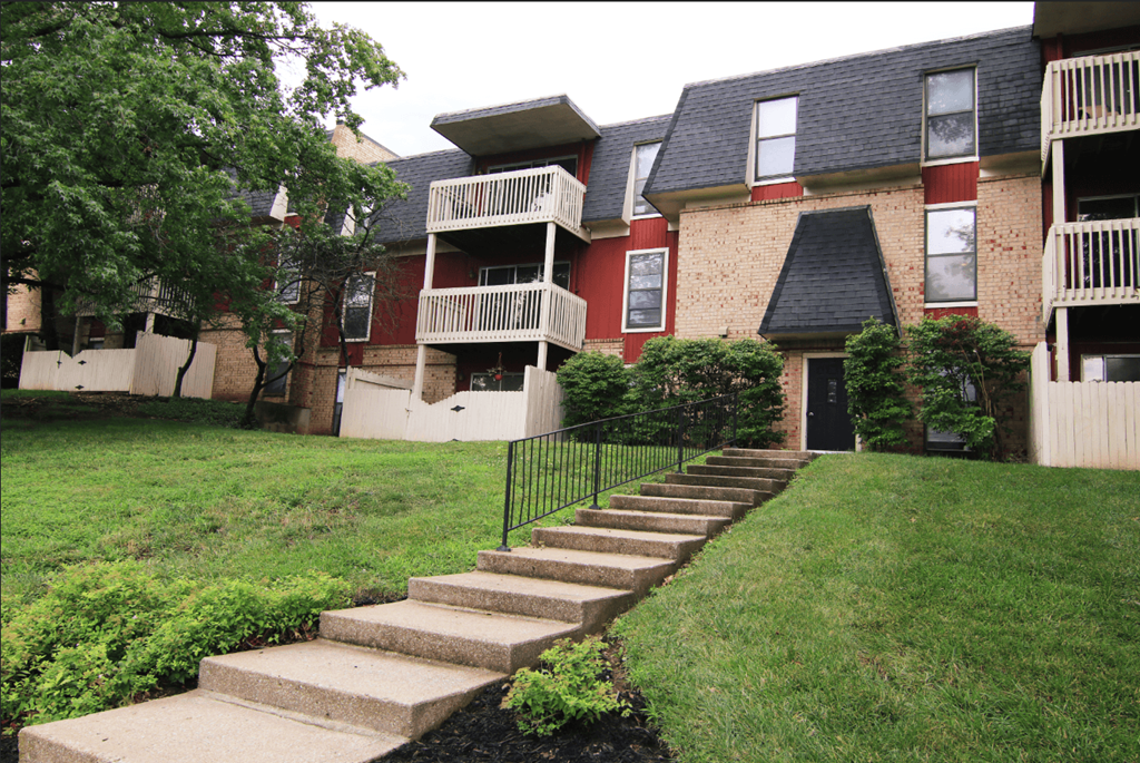 A building with a red and beige facade with a black iron fence and steps leading to the front door.