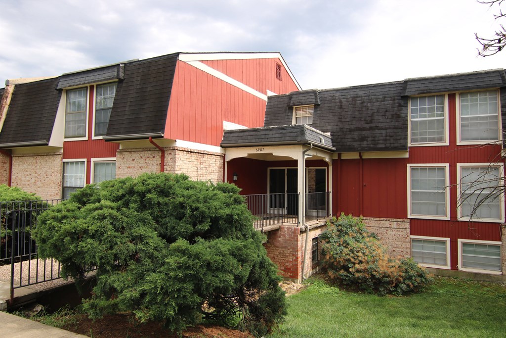 A red and white house with a black roof and a green bush in front.