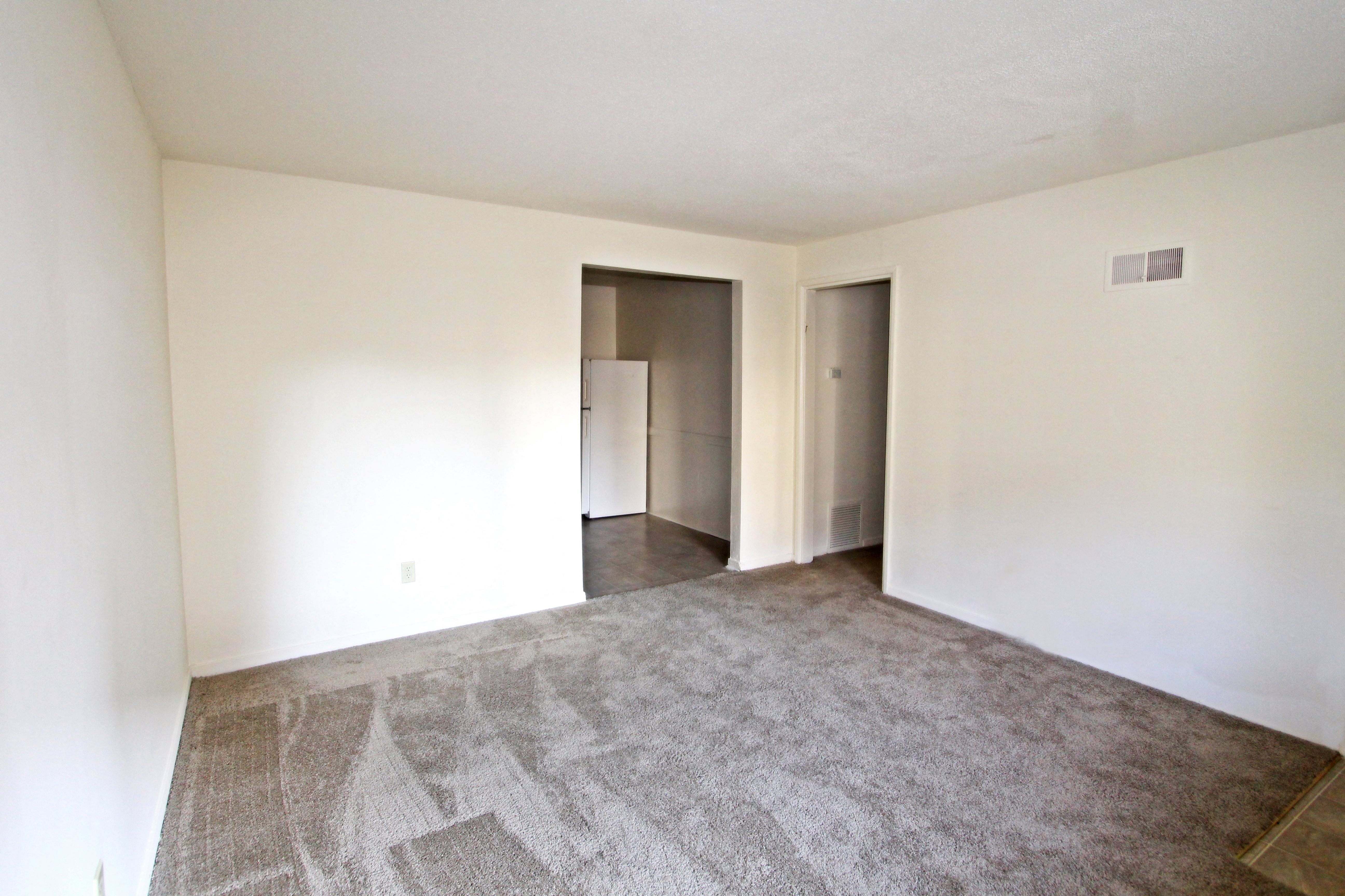 an empty living room with white walls and carpet and a door to a closet