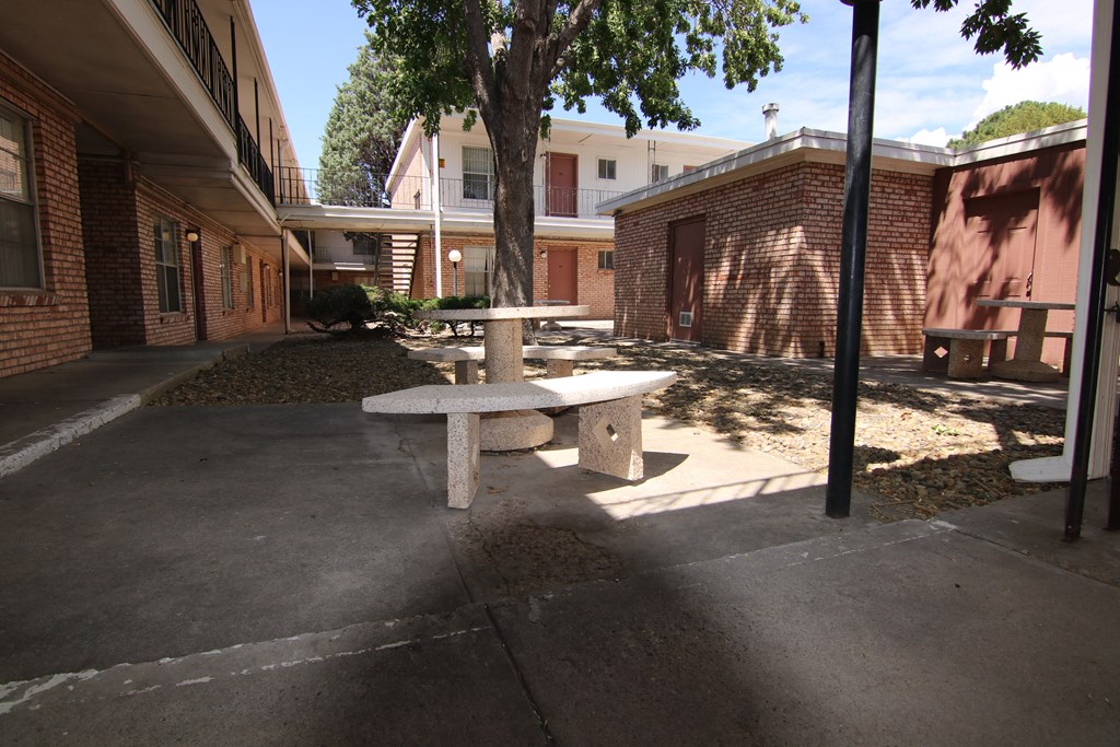 a concrete picnic table sits in the shade of a tree in front of a brick building