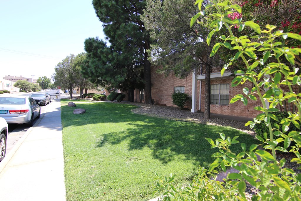 a grassy area with trees and bushes in front of a brick building