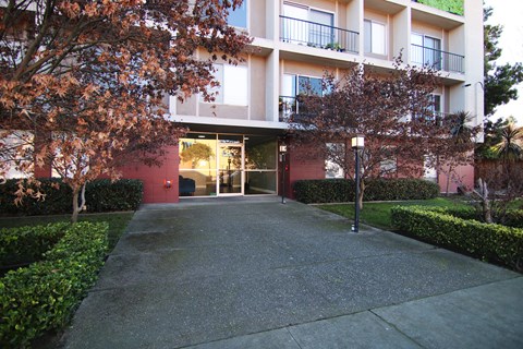 A building with a red door and windows is surrounded by trees and bushes.