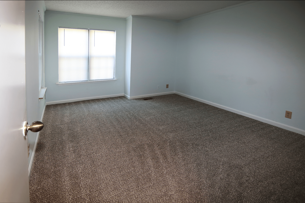 A room with a carpeted floor and a window with blinds.