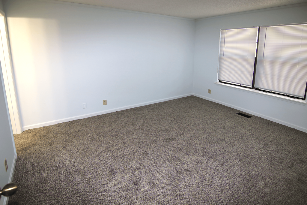 A room with a carpeted floor and a window with blinds.