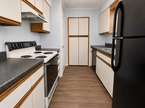 A kitchen with a black refrigerator, white cabinets, and a wooden floor.