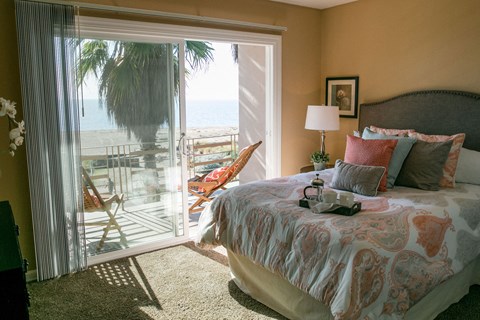 A bedroom with a large bed and a view of the beach through the sliding glass door.