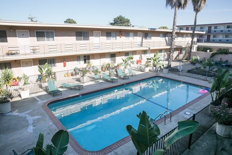 A swimming pool surrounded by chairs and plants in front of apartment buildings.
