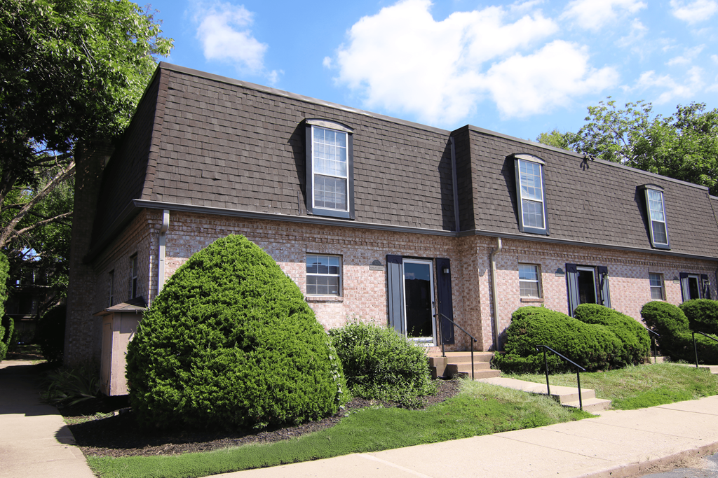 A house with a brown roof and a green bush in front.