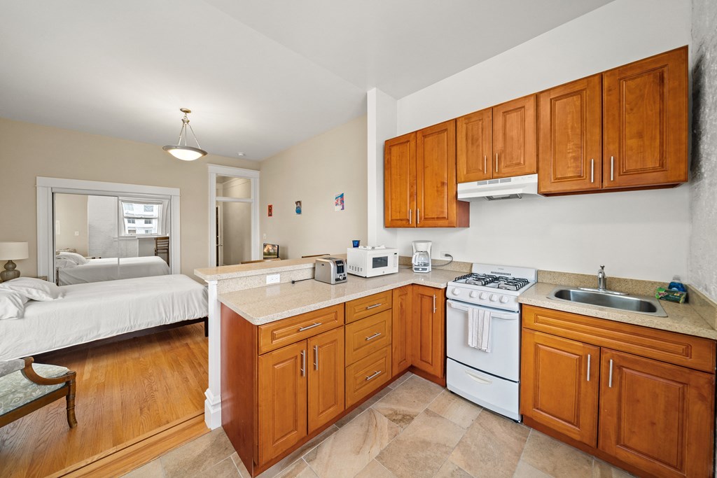 a kitchen with wooden cabinets and white appliances and a bedroom with a bed