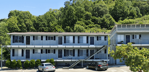A car is parked in front of a two-story apartment building.