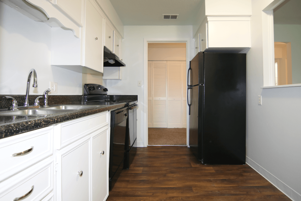 A black refrigerator sits in a kitchen with white cabinets and a black countertop.