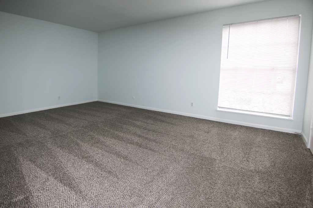 A room with a carpeted floor and a window with blinds.