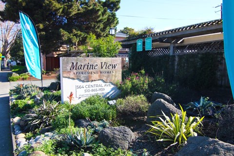 A sign for Marine View Apartment Homes is in front of a fence.