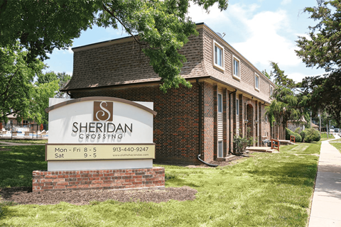 A sign for Sheridan Crossing is in front of a brick building.