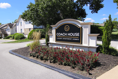 A sign for Coach House Luxury Apartment Homes is surrounded by plants.