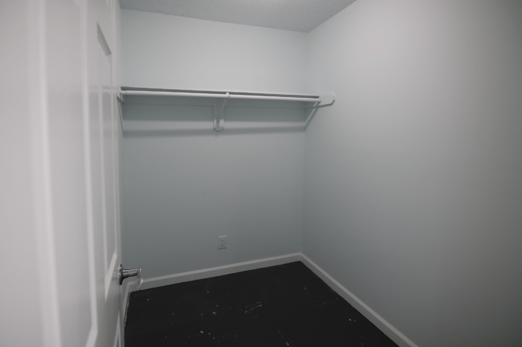 A white closet with a black floor and a white shelf.