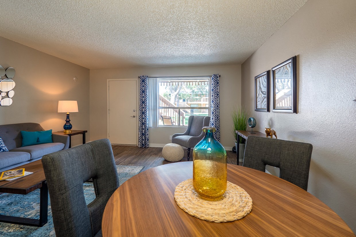 A living room with a grey couch, a grey chair, a wooden table with a yellow bottle on it, and a lamp on a side table.