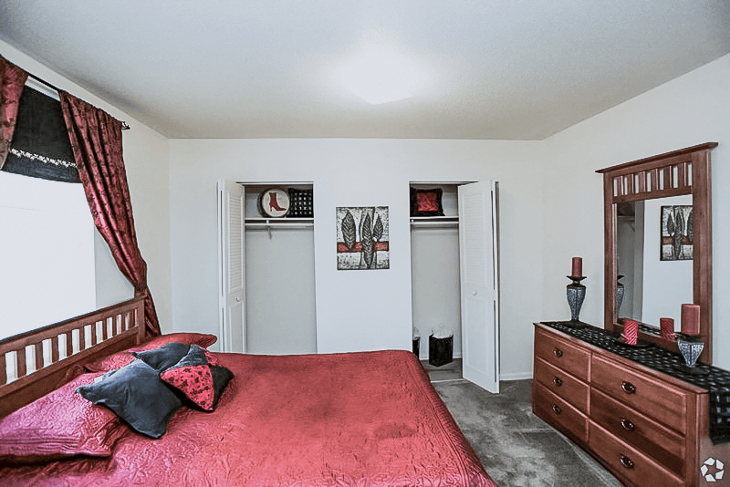 a bedroom with a red bed and a dresser at Gatehouse Apartments, Kansas City, MO, Missouri, 64134