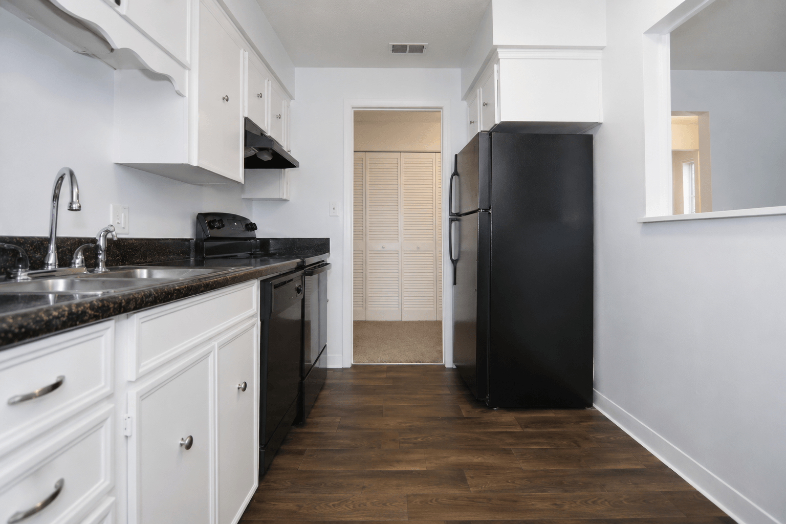 A black refrigerator stands in a kitchen with white cabinets and a black countertop.