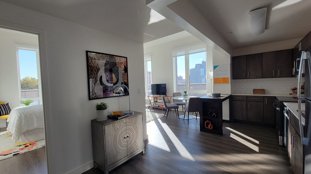 a living room and kitchen with a bed and a desk and a window