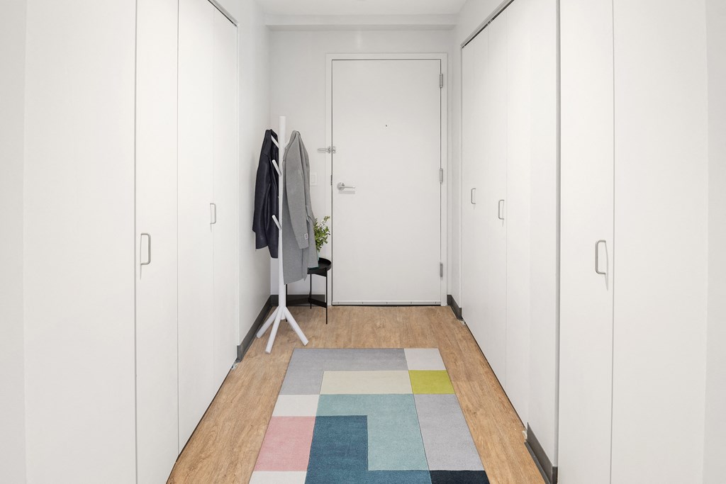 a long white hallway with white closets and a colorful rug