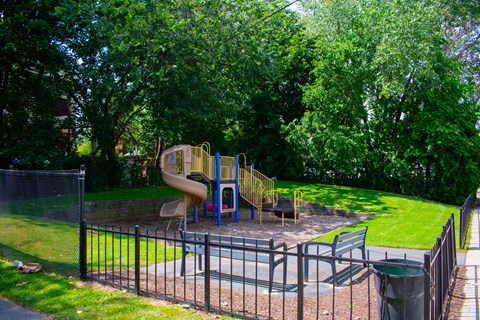 A playground with a yellow slide and a black fence.