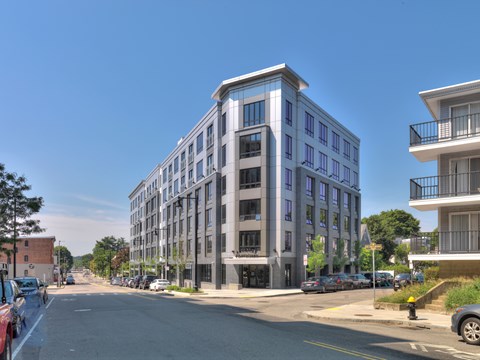 A street view of a modern multi-story building with cars parked on the side of the road.