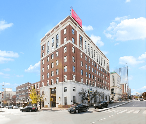 a tall brick building with a red sign on top of it on a city street