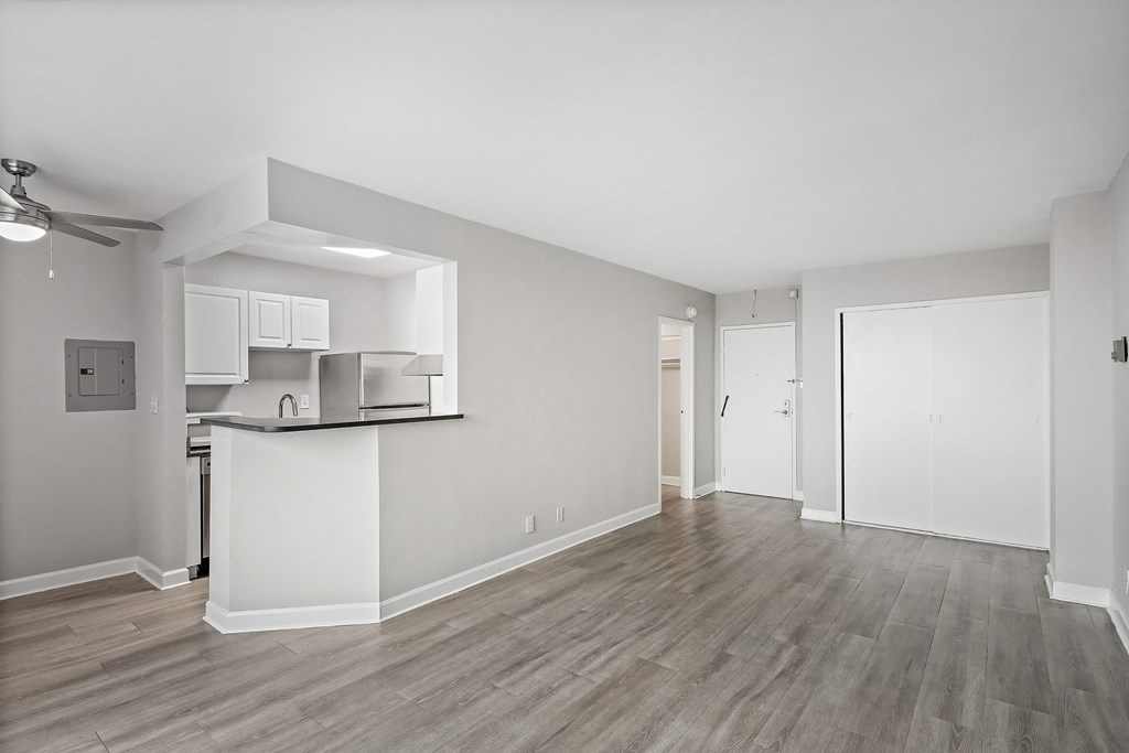 the living room and kitchen of an apartment with white walls and wood flooring