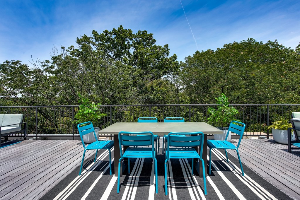 A table with blue chairs is set up on a wooden deck.