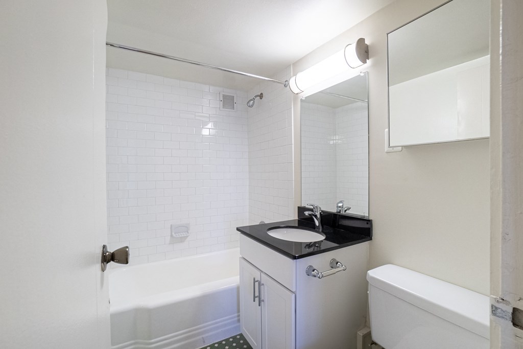 A white bathroom with a black counter top and a white tub.