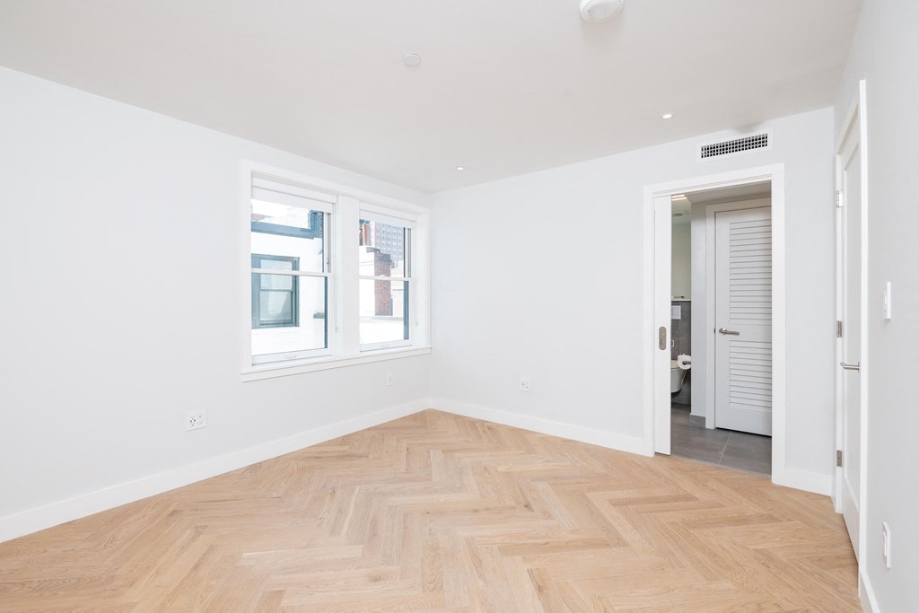 a bedroom with a hardwood floor and two windows