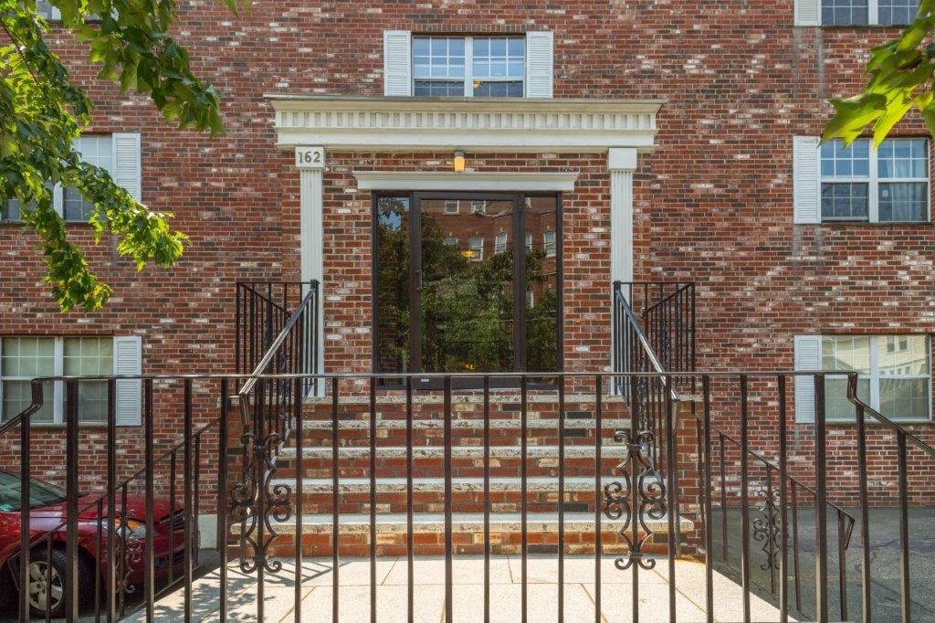 A red car is parked in front of a brick building with a black gate.
