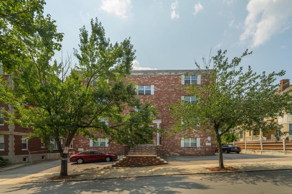 A red car is parked on the street in front of a brick building.