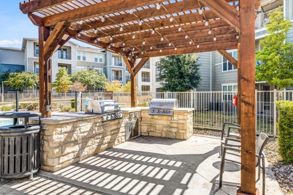 a patio with a stone wall and a wooden structure with a grill