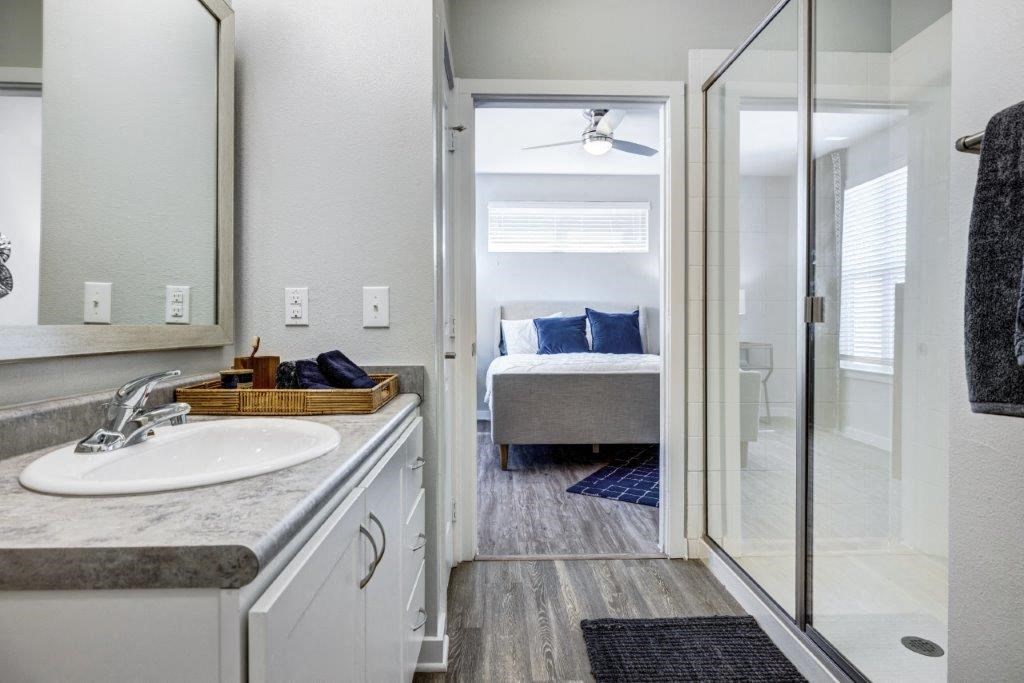 a bathroom with a shower and a sink and a bedroom