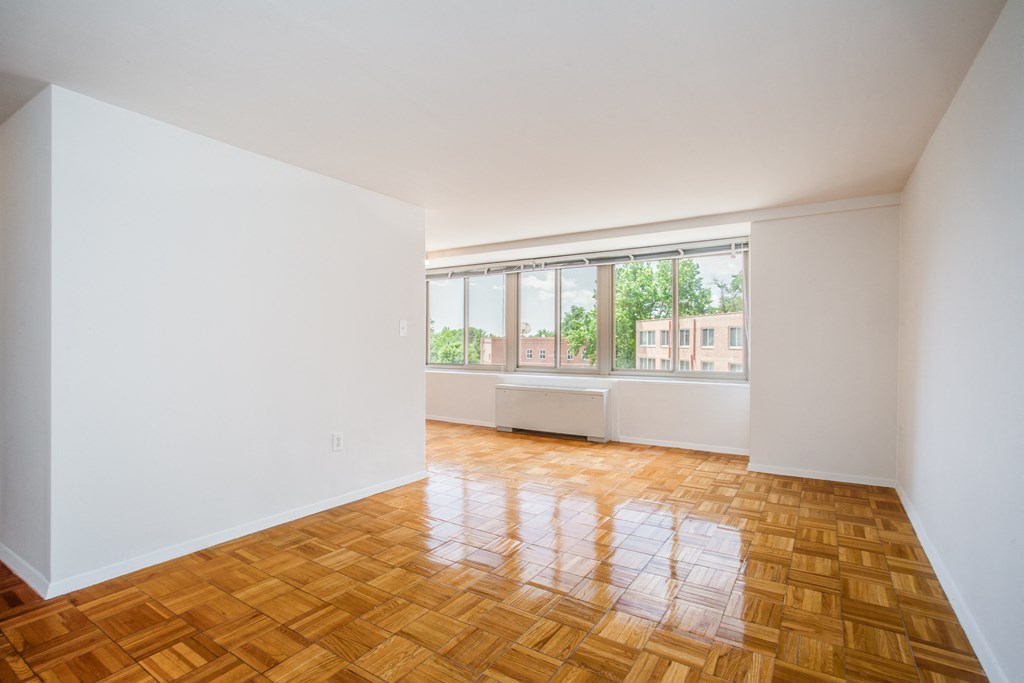 A room with a wooden floor and a window overlooking a building.