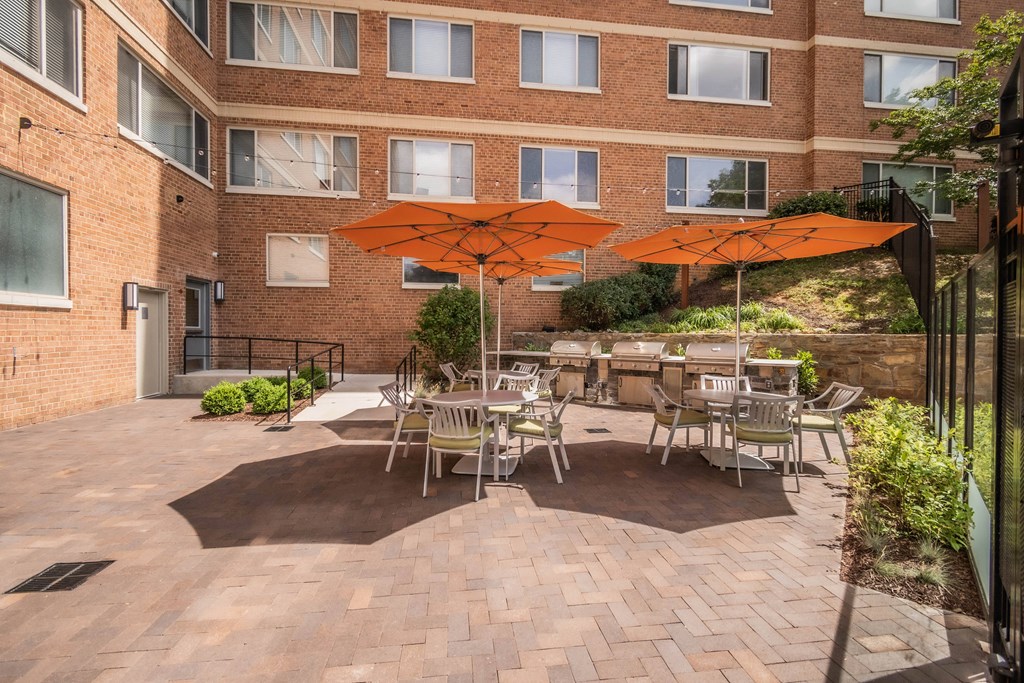 a patio with tables and umbrellas in front of a brick building
