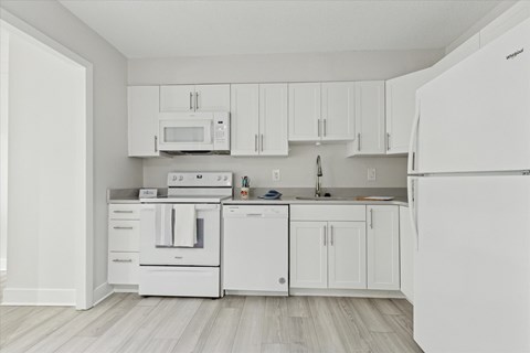 A white kitchen with a refrigerator, microwave, oven, and sink.